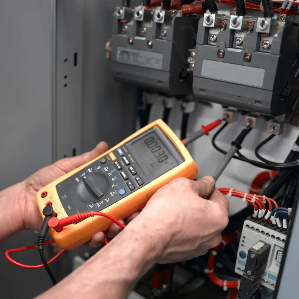 Electrical Fault Finding and Repair: Prevent Costly Faults Early 2 Hands holding a multimeter with test leads on a switchboard during electrical fault finding